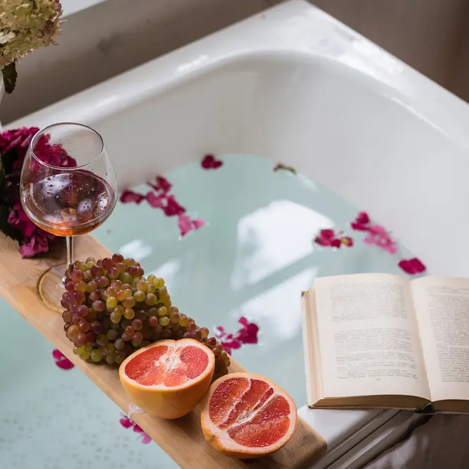 Glass of wine on a bath shelf with grapes, a book and grapefruit